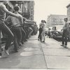 Jerome Robbins, crew, dancers: Exterior, city sidewalk: Jerome Robbins conducting warm-up class, row of male dancers in street clothes using basement railings for barre