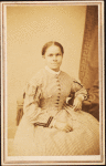 Studio portrait of unidentified seated woman wearing check dress.