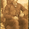 Studio portrait of unidentifed young man, seated on prop hay bale.