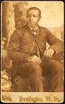 Studio portrait of unidentifed young man, seated on prop hay bale.