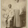 Studio portrait of a young couple, he seated, she with hand on his shoulder.