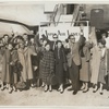Members of Graham company in street clothes standing and waving beside a Japan Airlines plane