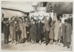 Members of Graham company in street clothes standing and waving beside a Japan Airlines plane