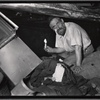 Man holding candle in basement surrounded by debris and rags: Manhattan