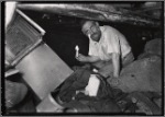 Man holding candle in basement surrounded by debris and rags: Manhattan