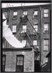 Rear view of tenement with children sitting on fire escapes