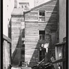 Debris strewn yard; wooden tenement; church steeple: Manhattan