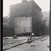 Vacant lot after demolition; wood frame houses with boarded windows