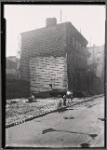 Vacant lot after demolition; wood frame houses with boarded windows