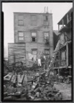 Rear of wooden buildings, debris in yard