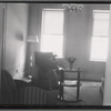 Woman seated in living room; newspaper with Rockefeller death headline