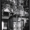 Tenement rear with fire escape; window awnings.