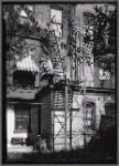 Tenement rear with fire escape; window awnings.