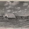 The present home of the Howard family. This family was photographed in April 1935. At that time they were on their way from Okla. to Calif. Camped in an open field. Mother pregnant with five starving children. Raw green onions were all that they had to eat. They were again photographed during the potato harvest. The baby was born then, and they had food. Now there is some prospect of a fairly decent home. A pile of odds and ends of lumber will eventually be a house. A truck garden is planted