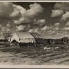 The present home of the Howard family. This family was photographed in April 1935. At that time they were on their way from Okla. to Calif. Camped in an open field. Mother pregnant with five starving children. Raw green onions were all that they had to eat. They were again photographed during the potato harvest. The baby was born then, and they had food. Now there is some prospect of a fairly decent home. A pile of odds and ends of lumber will eventually be a house. A truck garden is planted