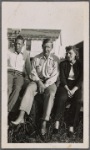 Auden flanked by Kallman and Rhoda Jaffe, sitting on fence in front of white cabin on Fire Island