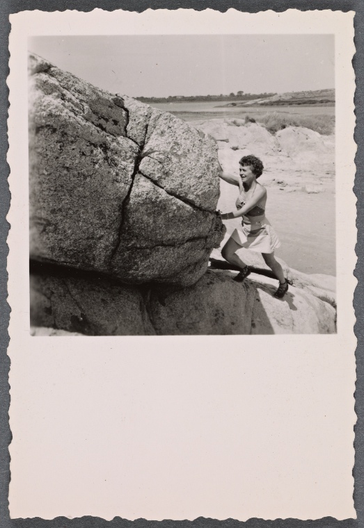 Picture of woman in summer clothing by the beach, pushing a boulder.