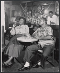 Claudia McNeil [sitting at left of table], John Bouie [sitting at right of table] and unidentified others in the stage production Simply Heavenly