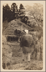 Rear view of man in straw raincoat (mino) and bamboo hat (kasa).