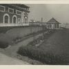 View of garden with greenhouse and arched trellises adjoining Ellis Island structure.