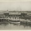 Buildings near Ellis Island pier; immigrants can be seen with trunks and luggage.