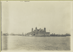A view of Ellis Island taken from the harbor. At the center is the A Immigration Station; one of the boats in the pier is the John E. Moore.