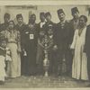 A group of immigrants, most wearing fezzes, surrounding a large vessel which is decorated with the star and crescent symbol of the Moslem religion and the Ottoman Turks.
