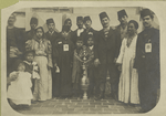 A group of immigrants, most wearing fezzes, surrounding a large vessel which is decorated with the star and crescent symbol of the Moslem religion and the Ottoman Turks.