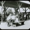 Corlear's Hook Park : boys and girls around table, swings beyond, ca. 1910s
