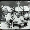 Corlear's Hook Park : boys and girls around table, swings beyond, ca. 1910s