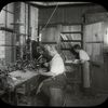 Enos Company : man works at workbench as another chooses books from shelves in corner, July 29, 1910