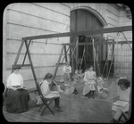 Women and girls reading near swingset where younger children are suspended in hammock like swings, July 1910