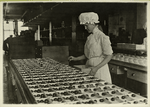 Woman in a mob cap sorting chocolates into wooden boxes