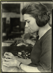 Woman worker appears to be pulling the woven tube of cloth used for insulating wires over the bare wire