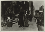 Entrance to a millinery supplies firm, showing several women on sidewalk, horse-cab and child playing in the trash