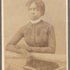 Unidentified young woman wearing gloves, leaning on prop fence.