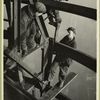 Three men welding an iron beam, high above the city]