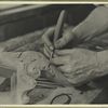 Hands of a wood carver putting finishing touches on a Chippendale chair or table leg]
