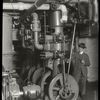 Central building, engine room : man, pipe in hand, standing beside machinery, ca. 1920s
