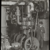 Central building, engine room : man, pipe in hand, standing beside machinery, ca. 1920s