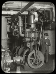 Central building, engine room : man, pipe in hand, standing beside machinery, ca. 1920s