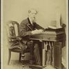 Charles Dickens. (Full length portrait, seated beside a desk and writing)