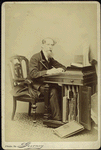 Charles Dickens. (Full length portrait, seated beside a desk and writing)