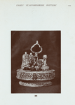 202. Circular cruet stand, with set of five bottles and two lids; variegated ware, brown, with splashes of blue, green and brown, on cream ground. Probably Whieldon. In the centre is a handle, and the body of stand is perforated. 9" x 7-1/2".