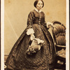 Portrait of older woman, standing, holding bonnet.