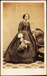 Portrait of older woman, standing, holding bonnet.