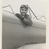 Nana Gollner seated in an open cockpit plane with aviator goggles and cap.
