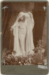 Full-length studio portrait of Loie Fuller holding veil over her head and pouring water from a shell.