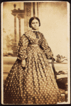 Portrait of young woman wearing patterned dress, with bow at neck.