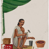 Seated male silversmith/jewelrymaker with small jewellry on red rug, holding tools